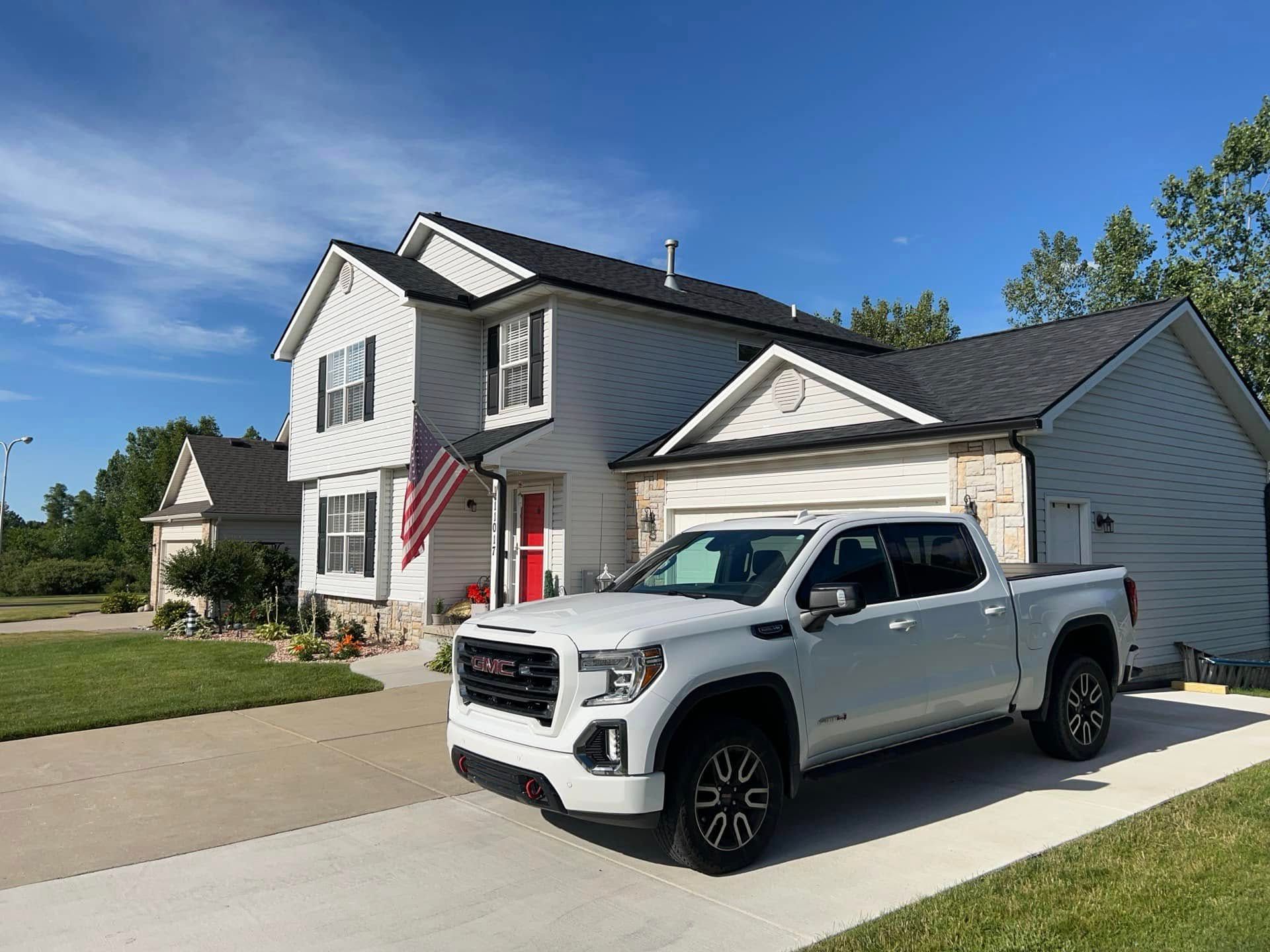 A white truck is parked in front of a white house.