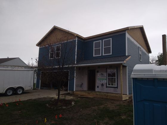 A house under construction with a blue portable toilet in front of it
