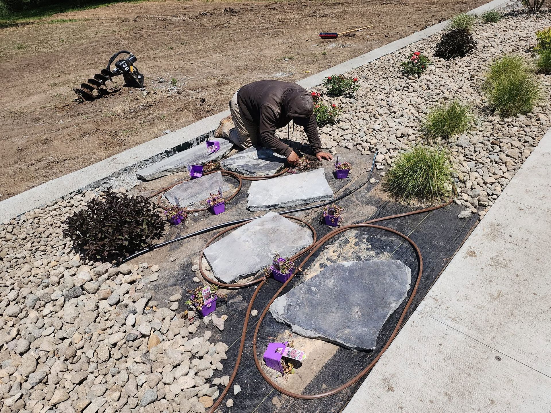 Worker installing landscaping stones and mulch in a garden bed beside a sidewalk