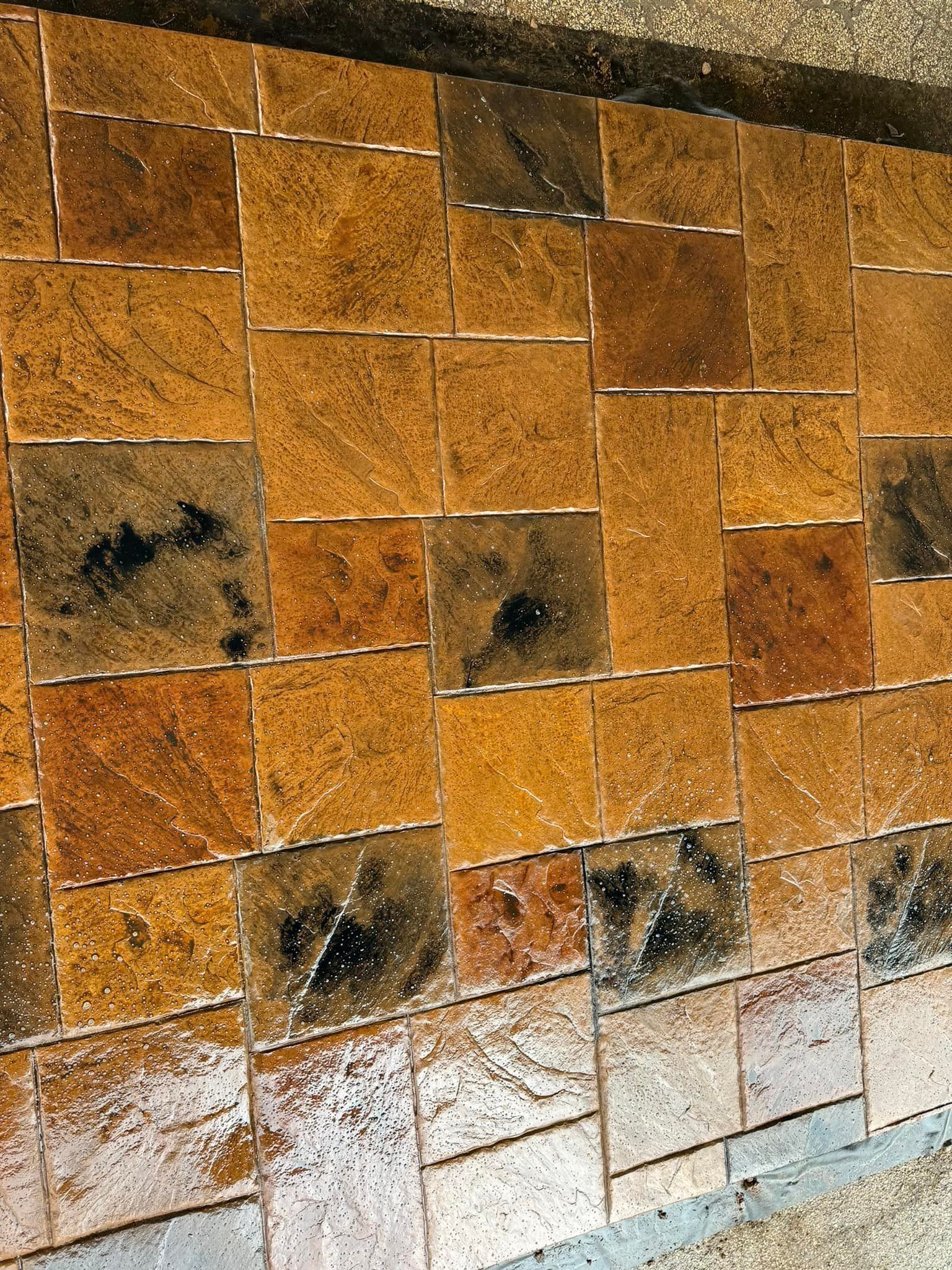 Close-up of square, textured, tan and brown tiles laid in a grid pattern; some tiles appear wet with dark spots.