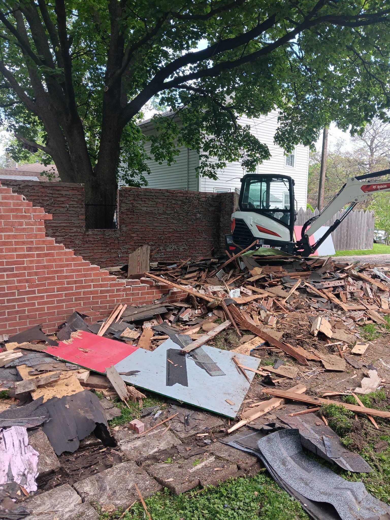 Bobcat operating near a brick wall, wood debris scattered around.