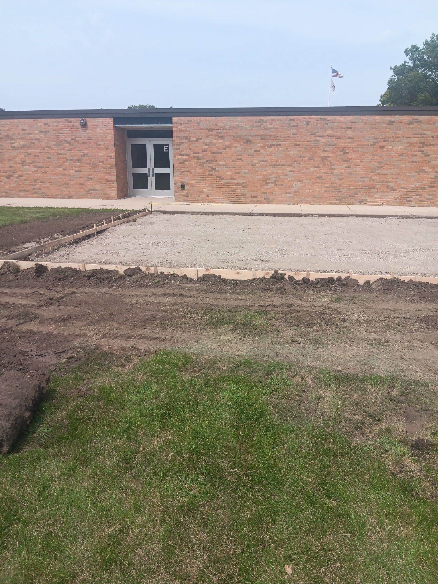 Exterior of a brick building with a door, gravel path, and freshly dug dirt in foreground.