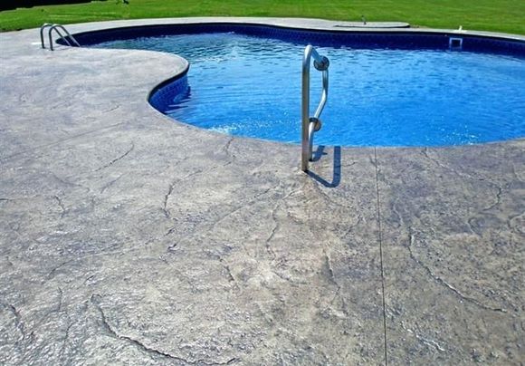 Stamped concrete patio with brown coloring next to grass, a white door, and a black fence.