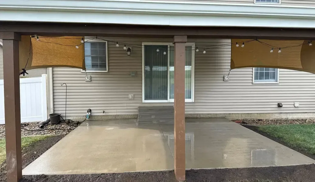 Stamped concrete patio, brown with darker lines, next to grass and white building with door.