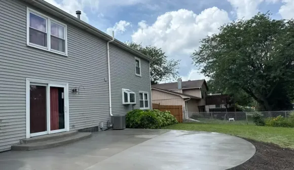 Stamped concrete patio with brown coloring next to grass, a white door, and a black fence.
