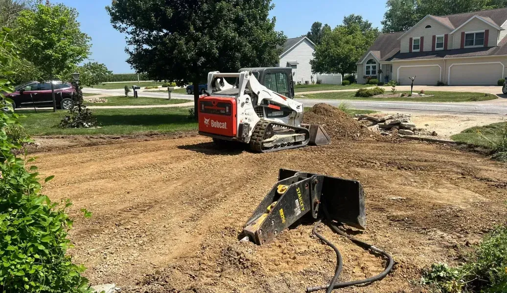 Construction vehicle demolishing concrete in front of an apartment building on a cloudy day.