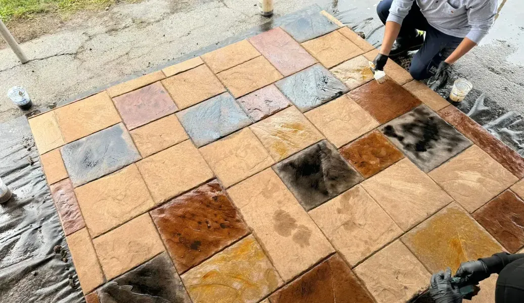 Man applying sealant to a newly laid patio of colorful stone tiles.