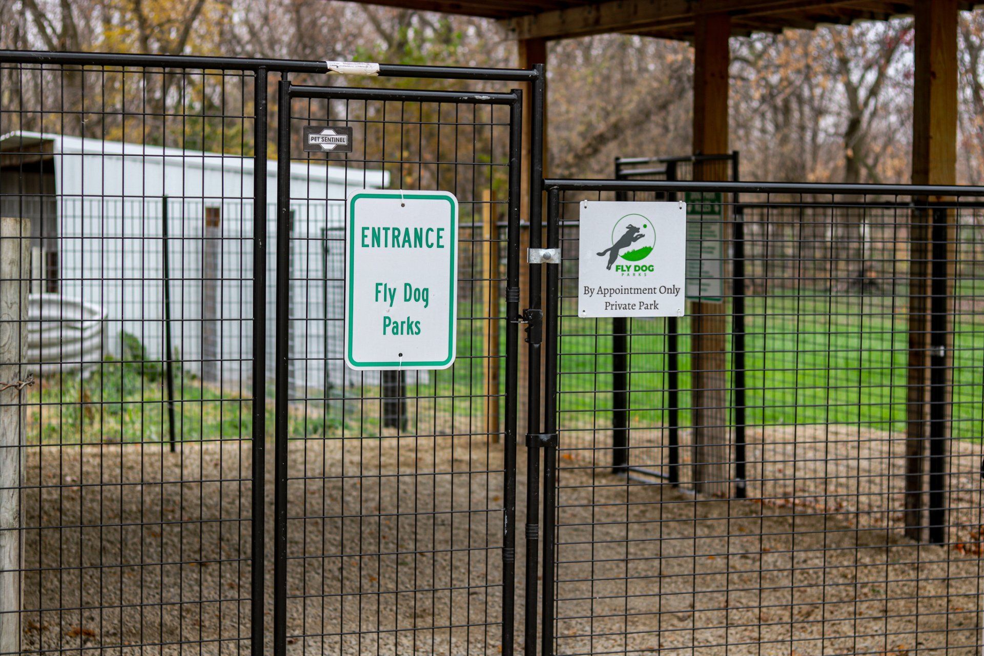 A fence with signs on it that say entrance and fly dog park.