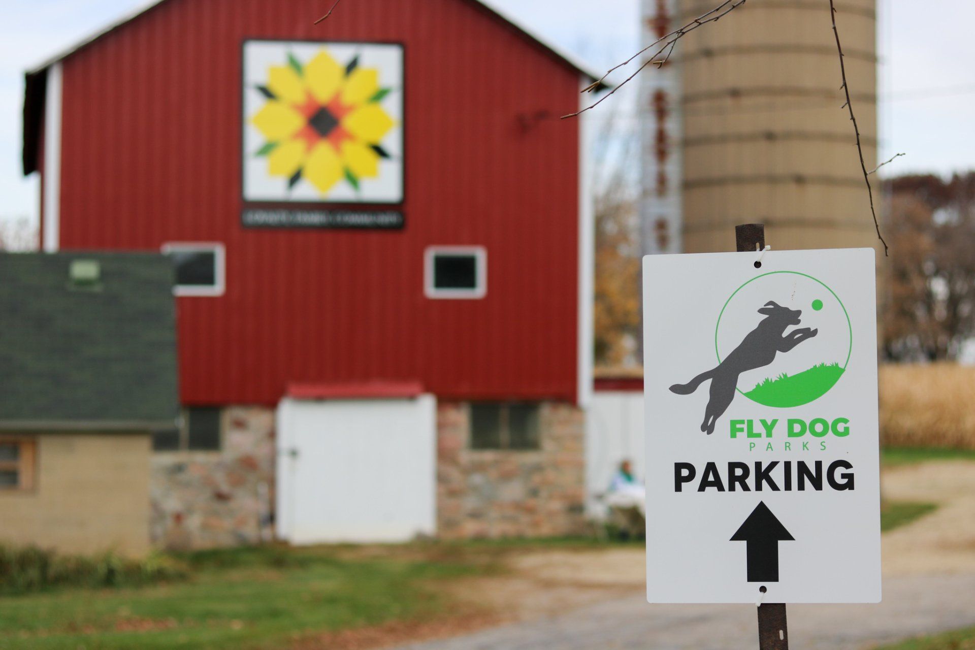 A fly dog parking sign in front of a red barn