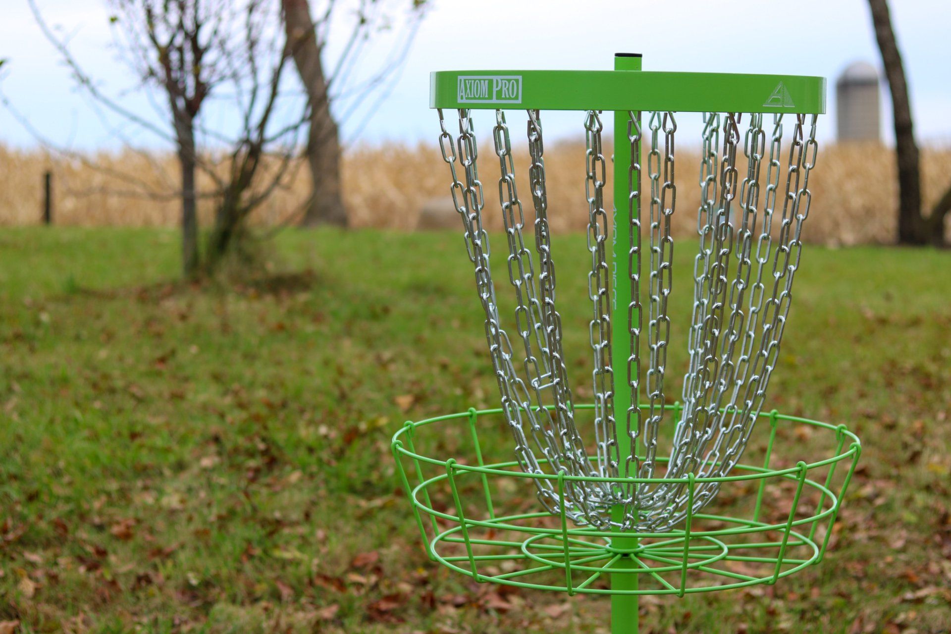 A green frisbee golf basket is sitting in the middle of a grassy field.