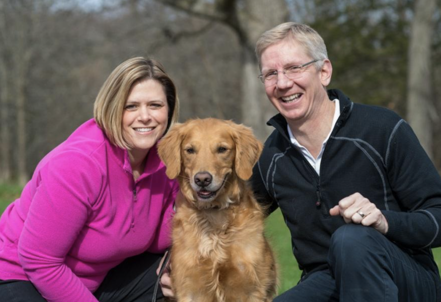 A man and woman are posing for a picture with their dog.