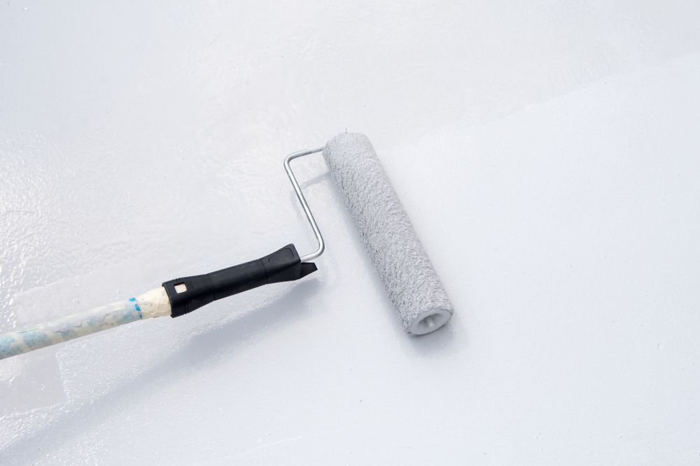A Man is Painting a Wall With a Roller in an Empty Room — Brushworks Painting In North Albury, NSW.
