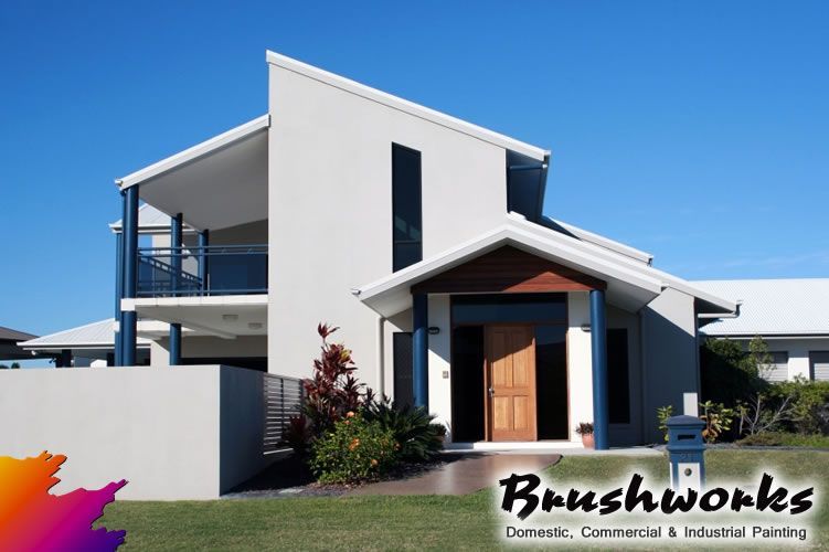 A Man is Standing on a Ladder Painting the Side of a Building — Brushworks Painting In Thurgoona, NSW.