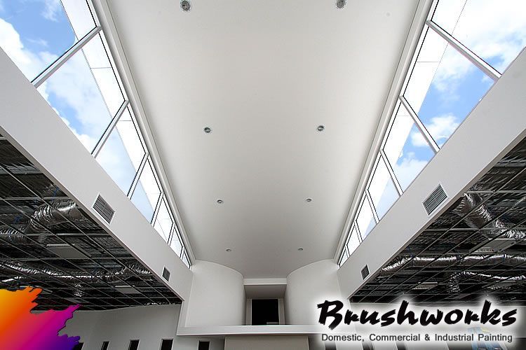 Interior view of a modern building with a long, white ceiling and large skylights. The sky is visible through the windows — Brushworks Painting In North Albury, NSW.