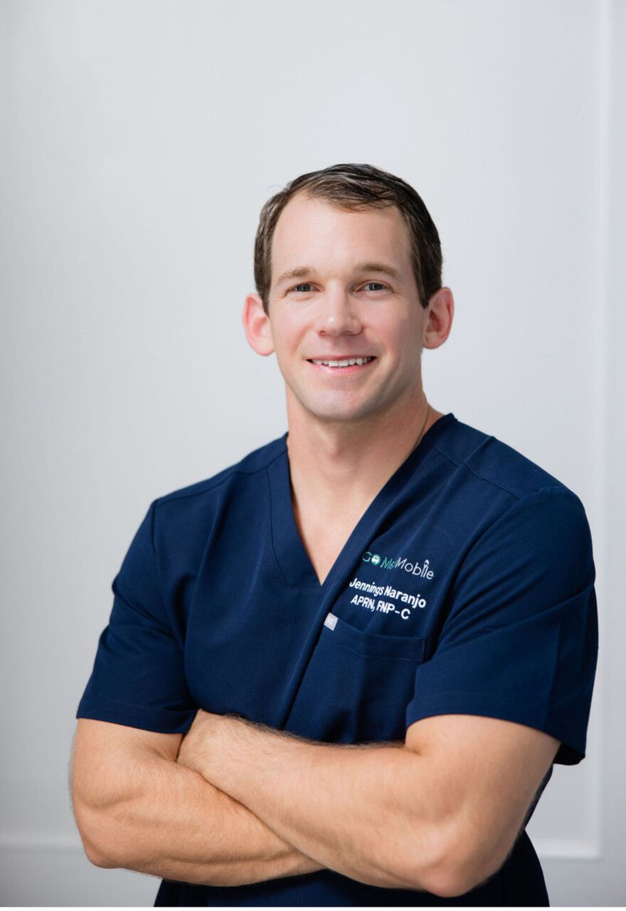 A man in a blue scrub is smiling with his arms crossed
