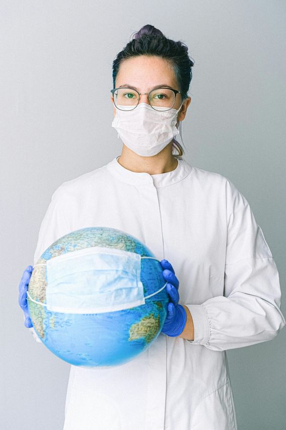A woman wearing a mask and gloves is holding a globe.