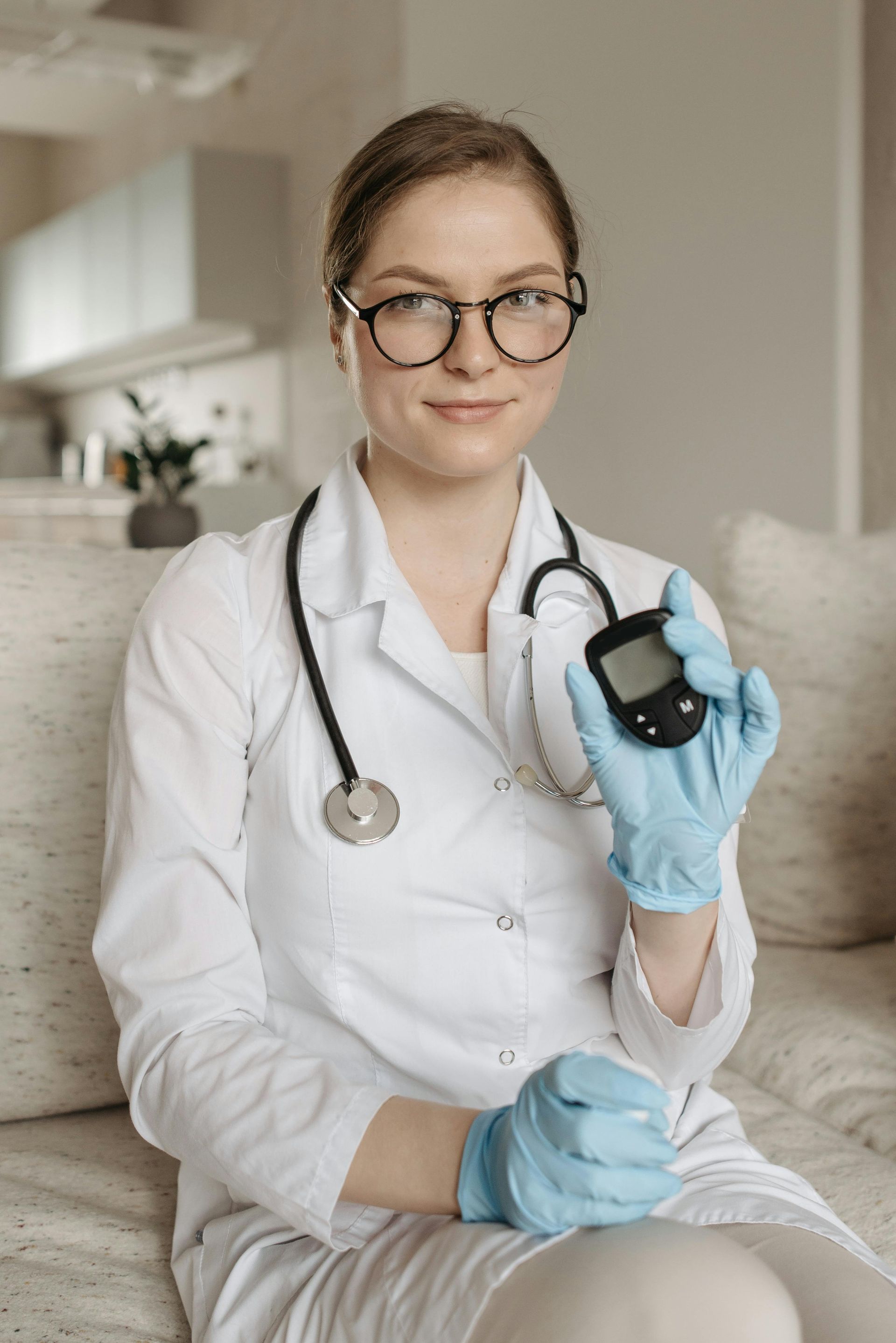 A female doctor is sitting on a couch holding a glucose meter.