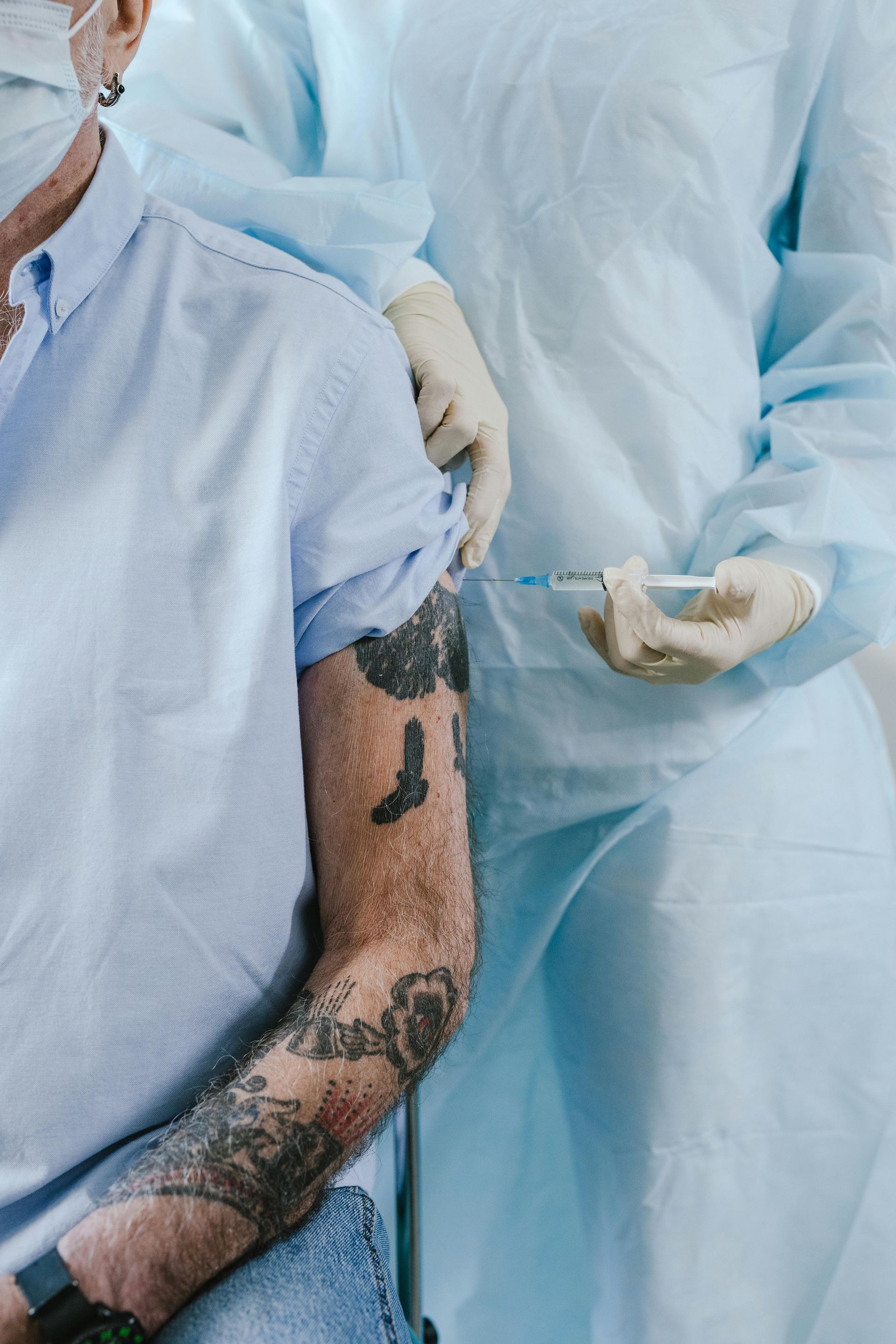 A man with tattoos is getting a vaccine in his arm.