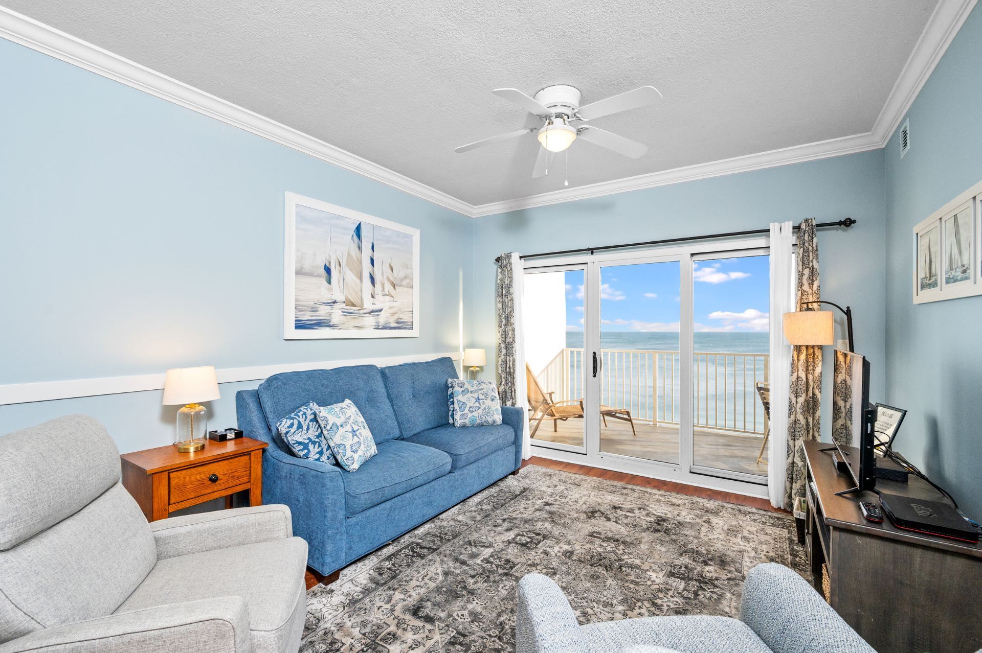 A living room with a blue couch , two chairs , a television and a ceiling fan.