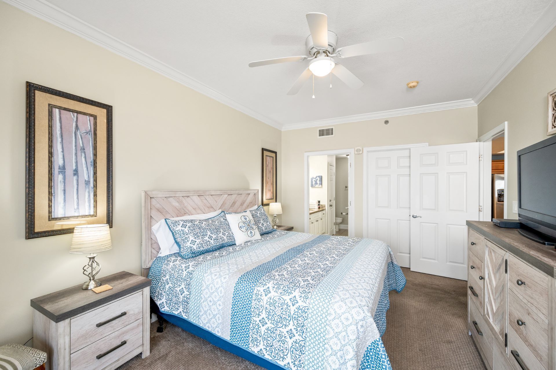A bedroom with a king size bed , dresser , nightstand , television and ceiling fan.