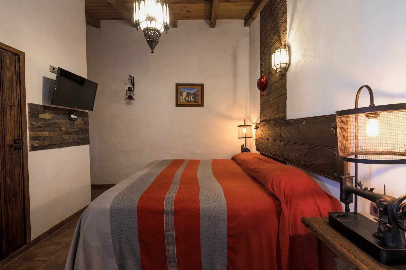Un dormitorio con paredes blancas, techo de madera, ropa de cama a rayas rojas y grises