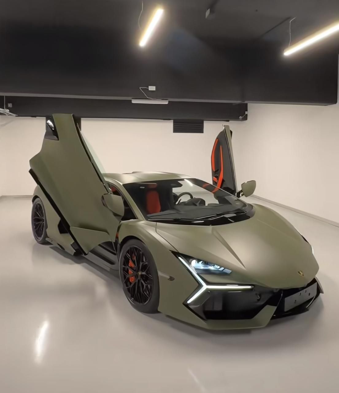 A green sports car is parked in a garage with its doors open