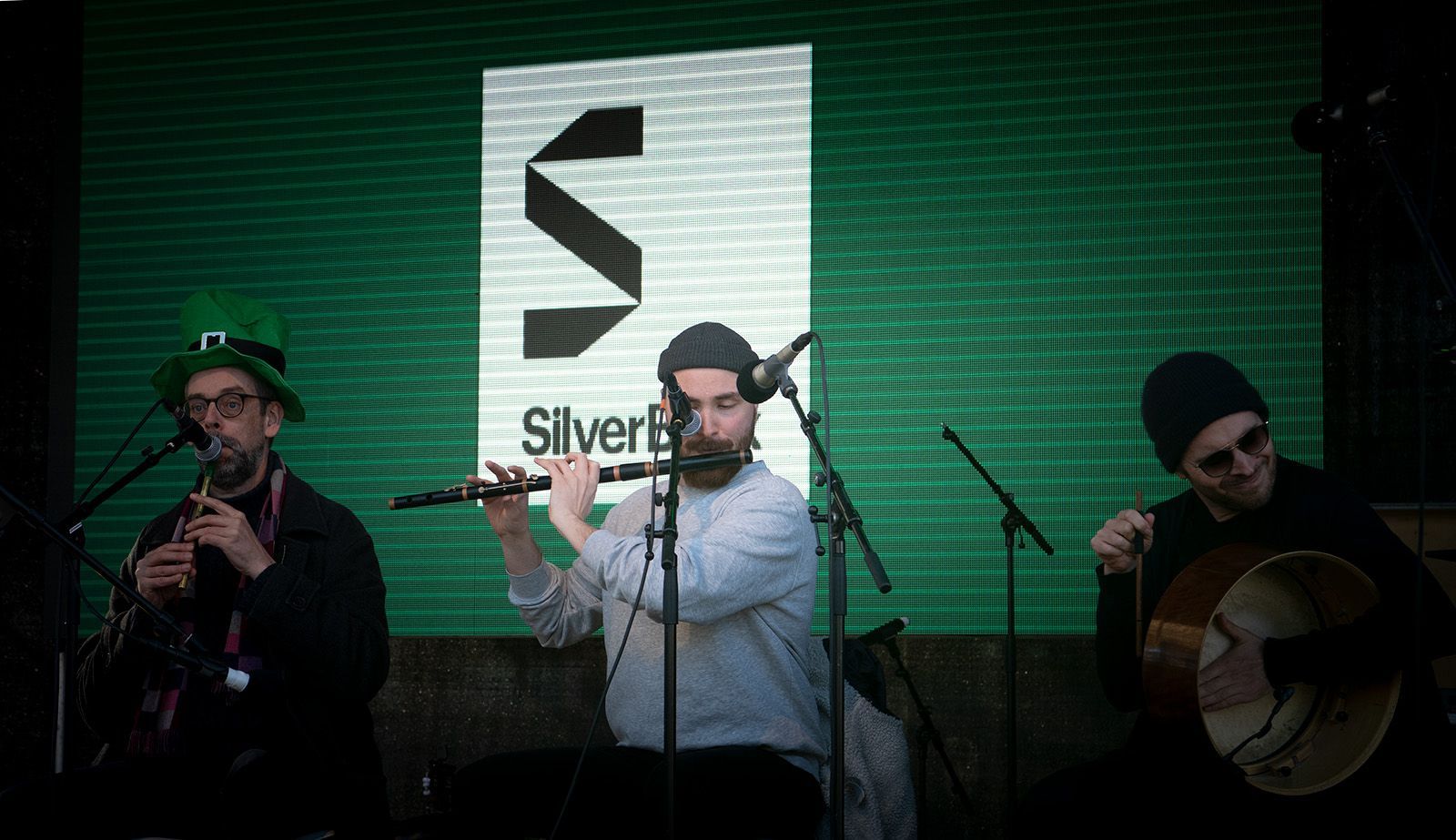 A man is playing a flute in front of a sign that says silver