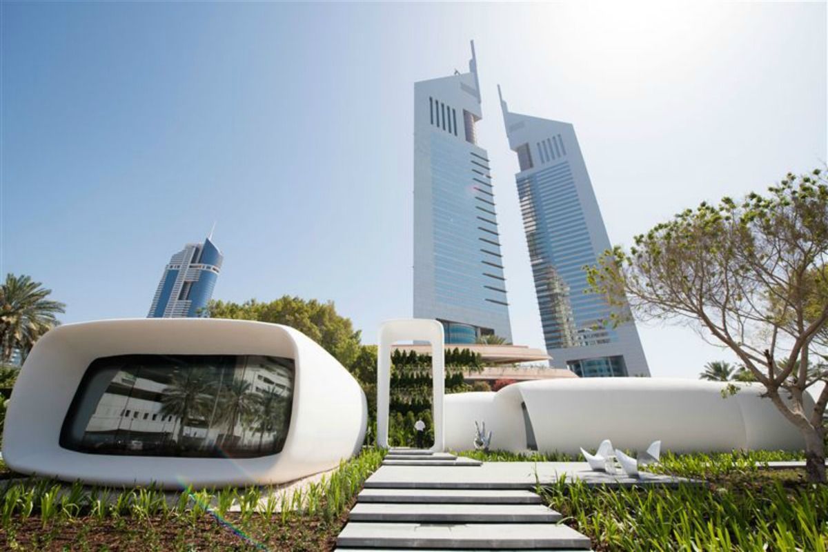 A white building with a walkway leading to it in front of a tall building.