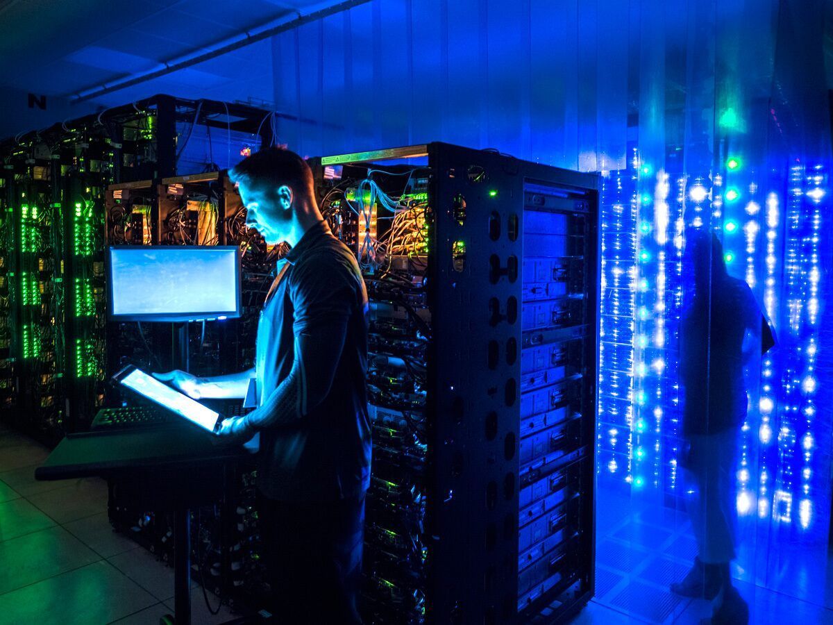 A man is working on a computer in a server room.
