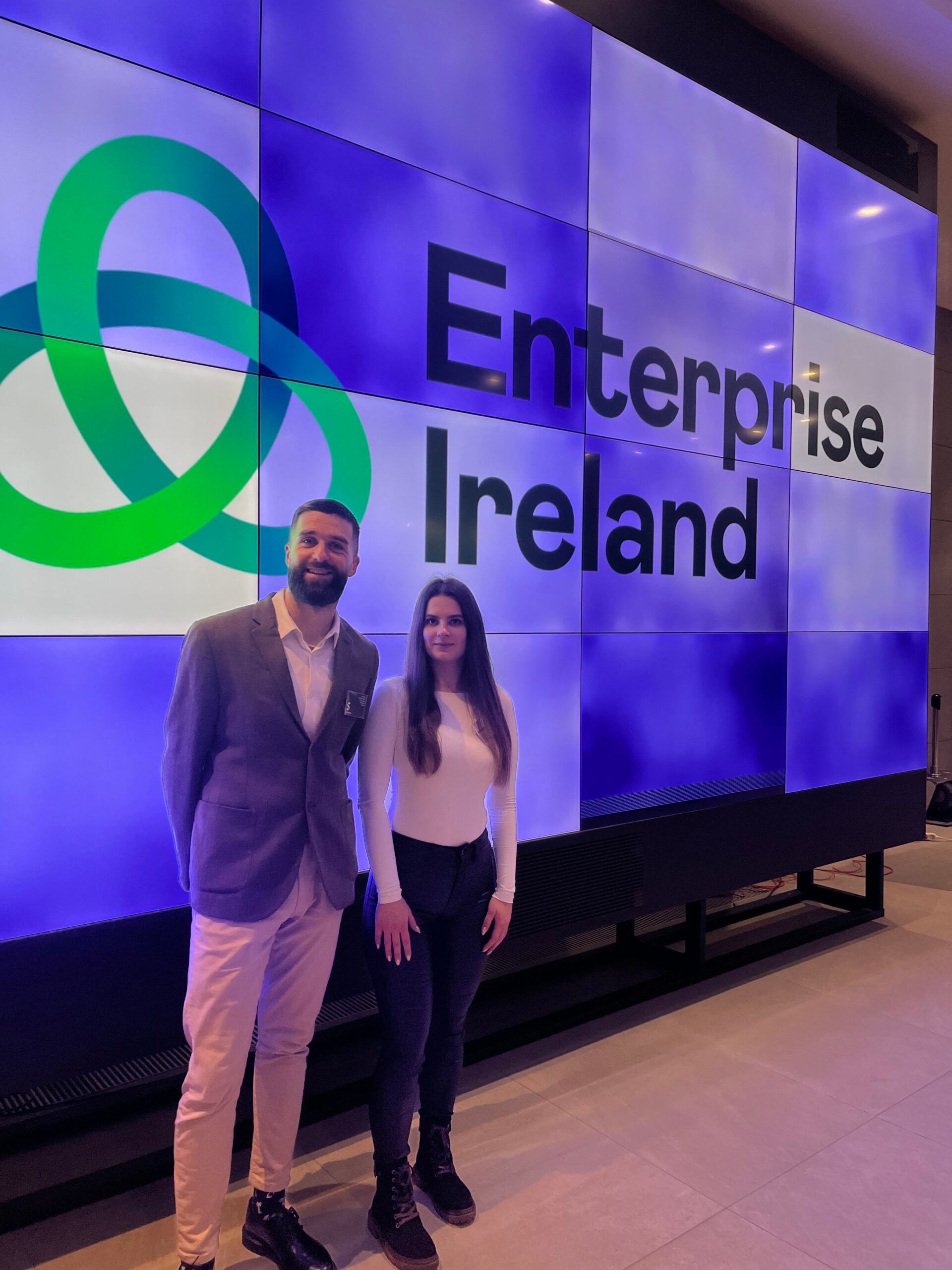 A man and a woman are standing in front of a large screen that says enterprise ireland