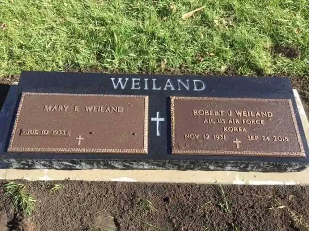 Weiland family gravestone in a grassy cemetery, with two bronze memorial plaques.