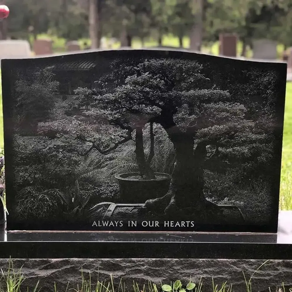 Black granite gravestone engraved with a tree and the words “Always in our hearts.”