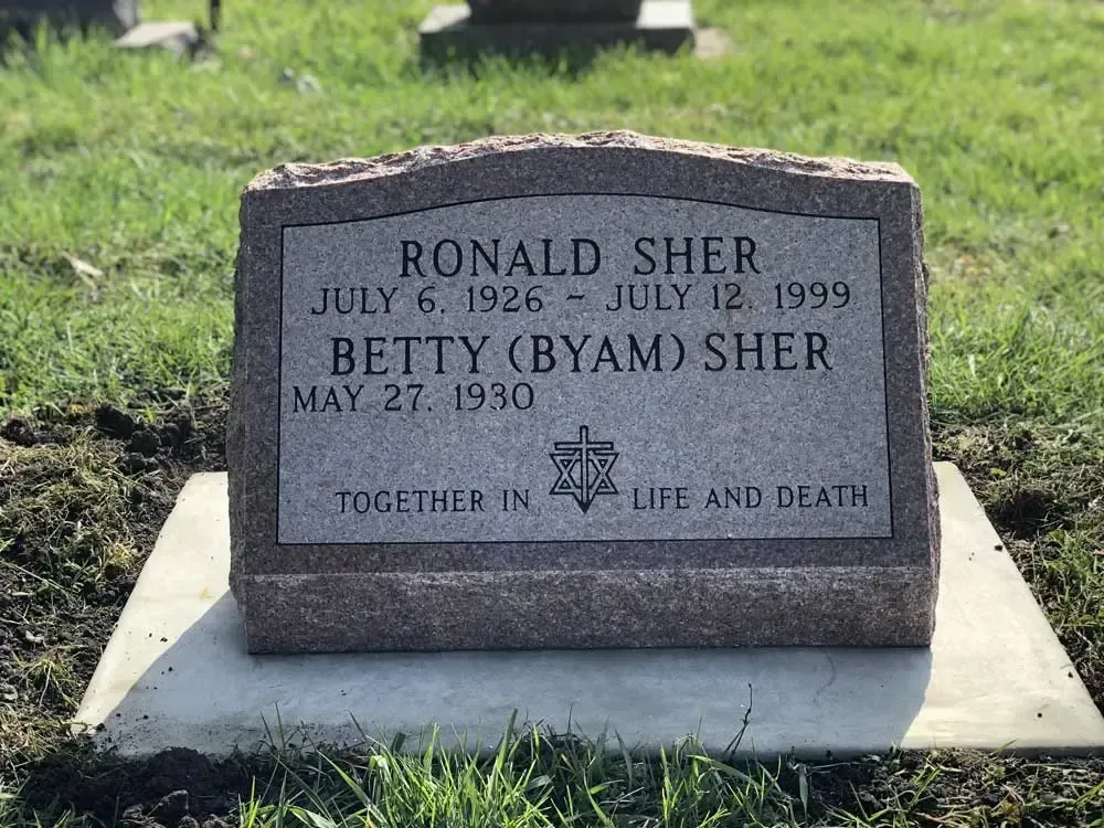 Gravestone for Ronald Sher and Betty (Byam) Sher in a grassy cemetery, with dates engraved.