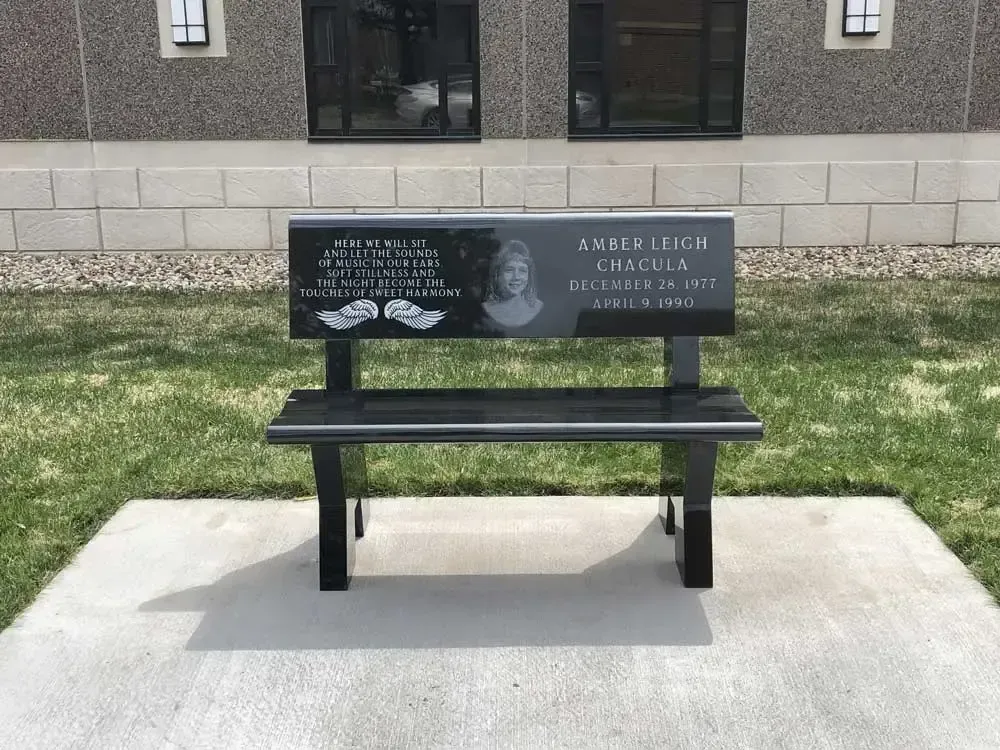 Memorial bench with a black engraved plaque and white handprints in front of a building
