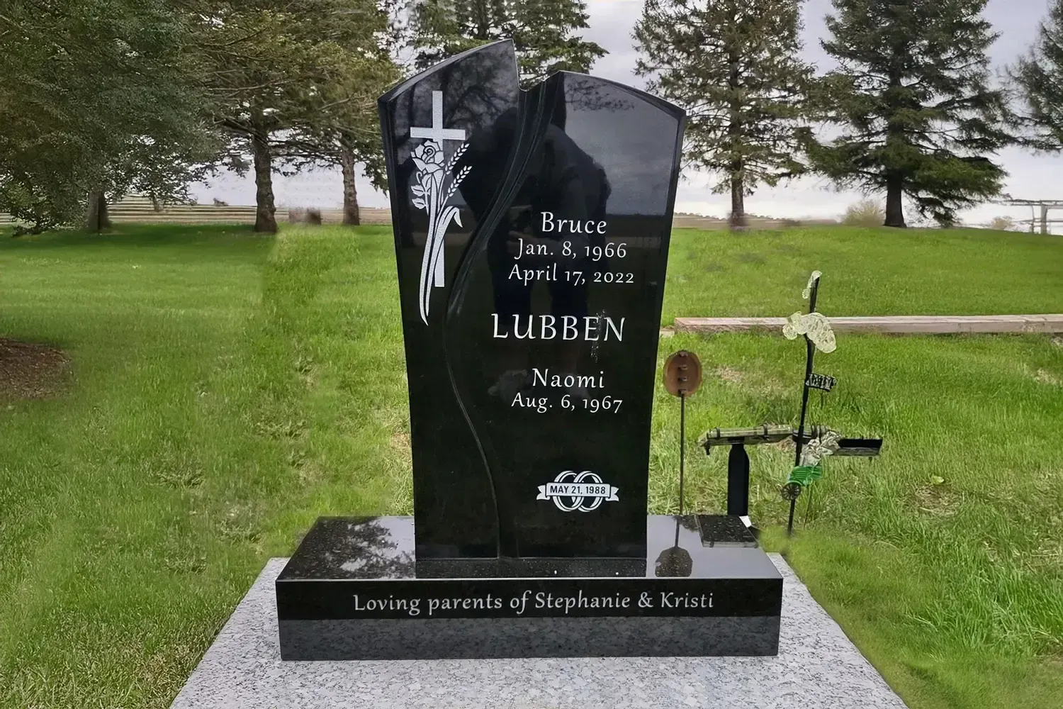 Black granite gravestone with white cross in a green cemetery lawn.