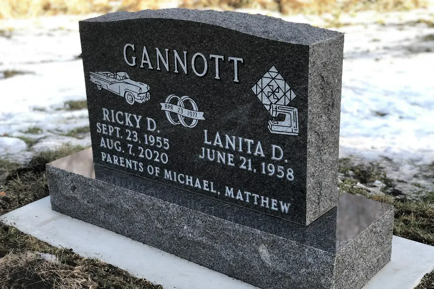 Black granite double gravestone with engraved names and dates in a snowy cemetery