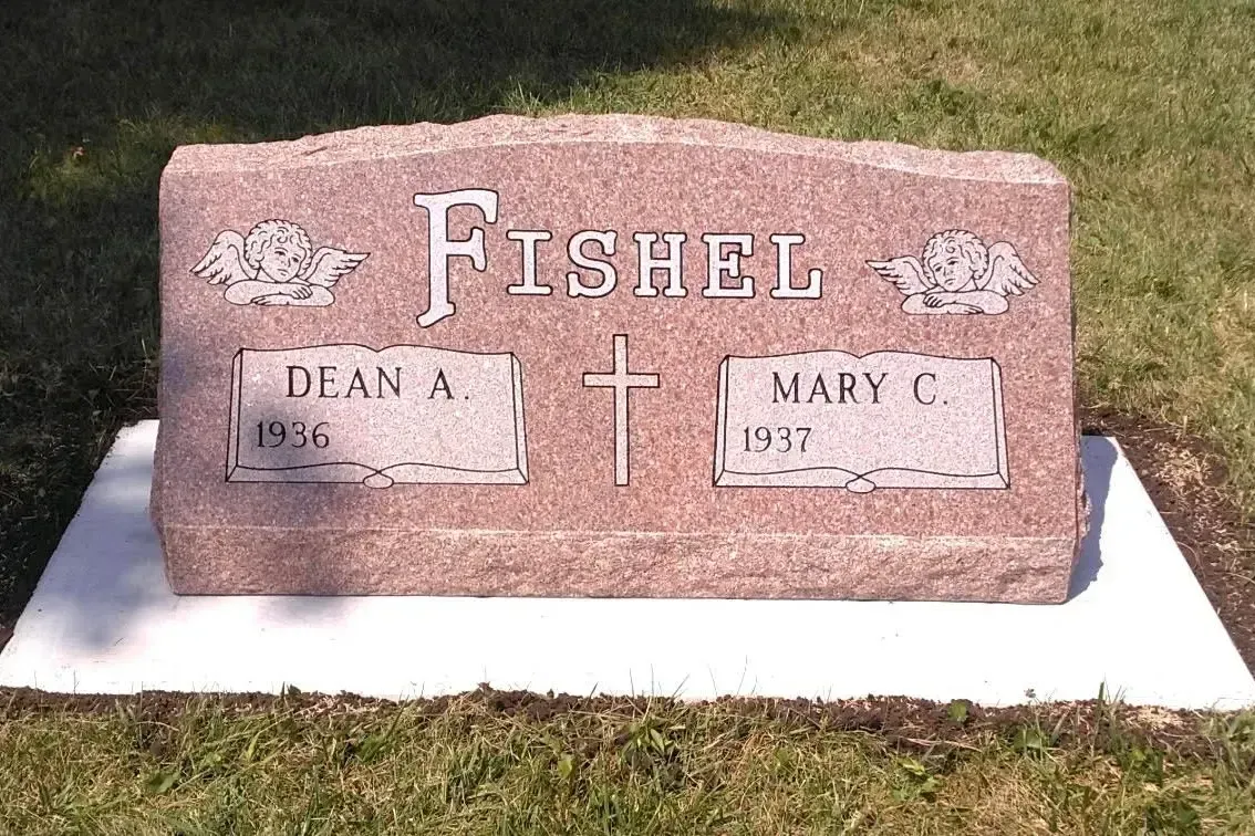 Pink granite double headstone engraved “FISHEL” with two name plaques in a grassy cemetery.