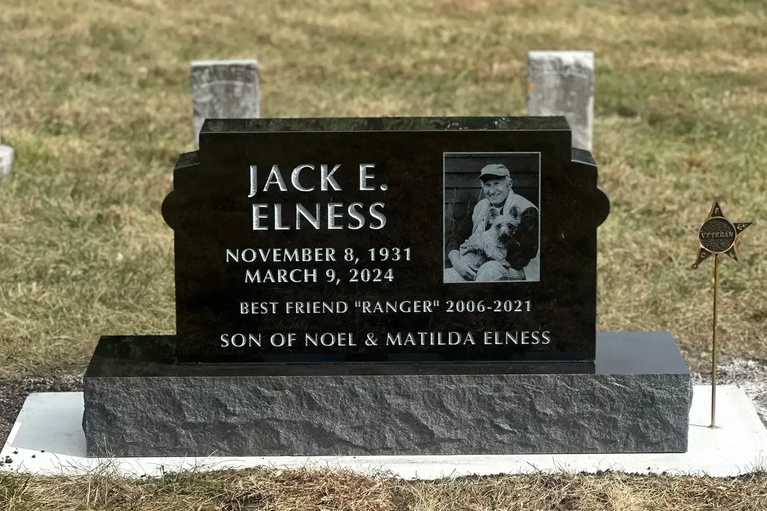 Black granite memorial headstone for Jack E. Elnes in a grassy cemetery.