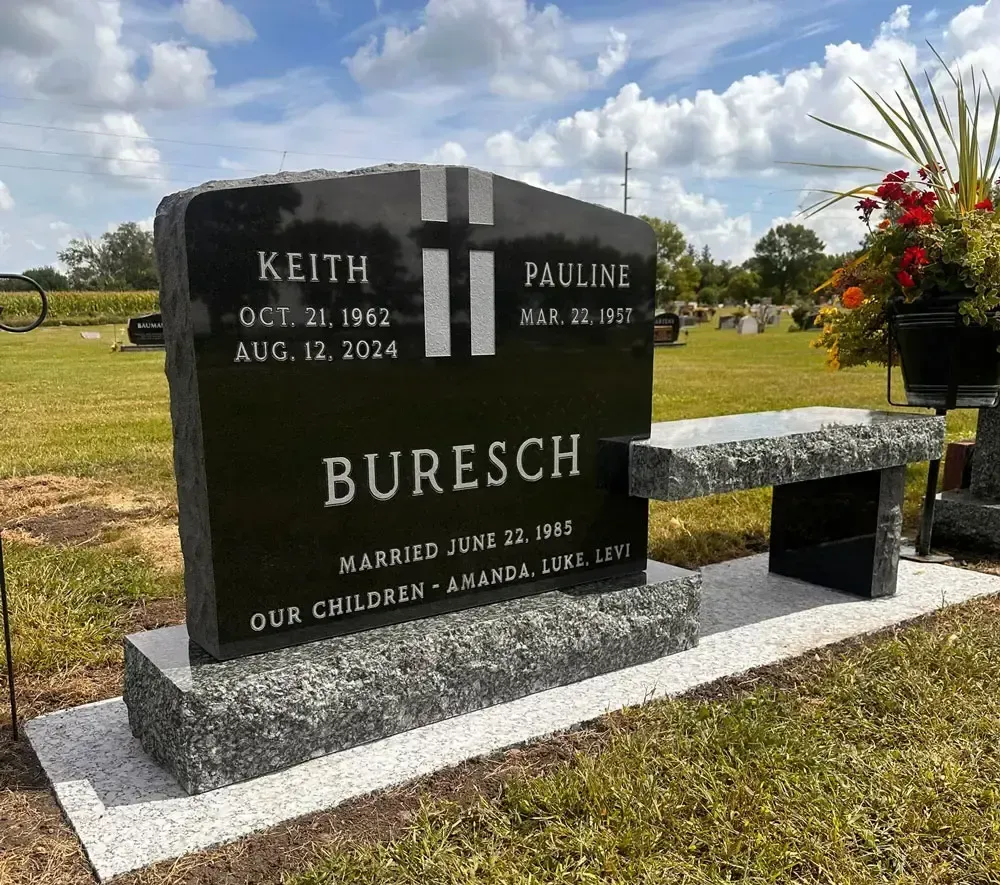 Black granite Buresch gravestone with flowers in a cemetery under a cloudy sky