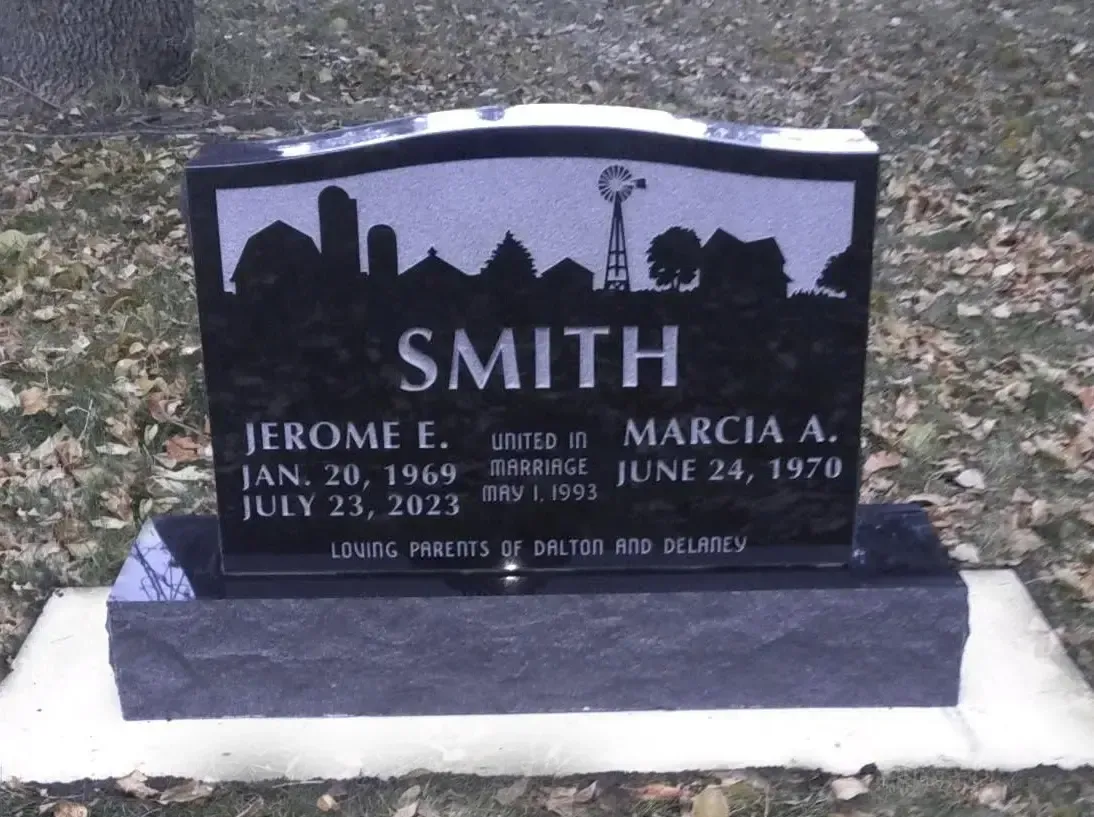 Black gravestone with white lettering and skyline silhouette in a cemetery, marked SMITH.