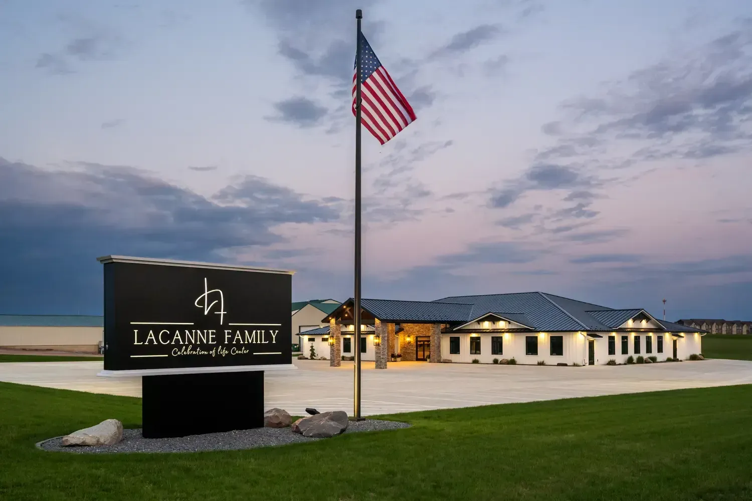 Lacanne Family sign and American flag at a lit building at dusk