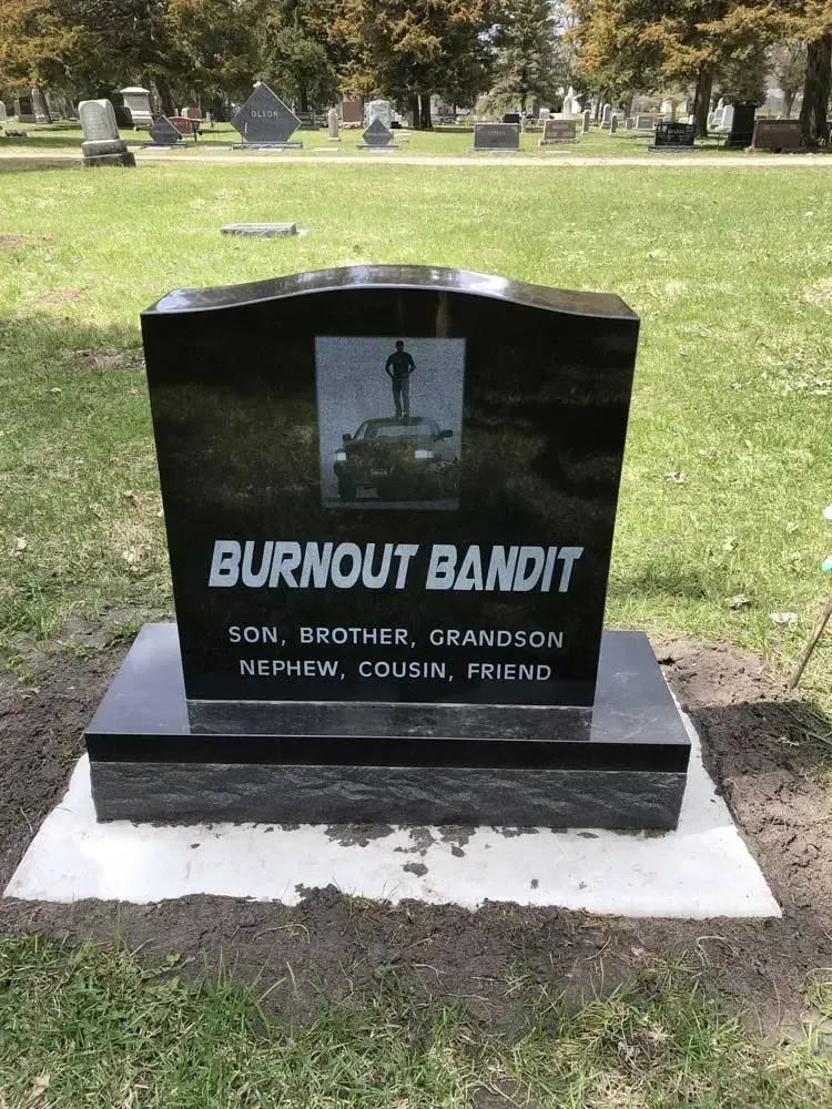 Black granite memorial headstone with flowers in a grassy cemetery park.