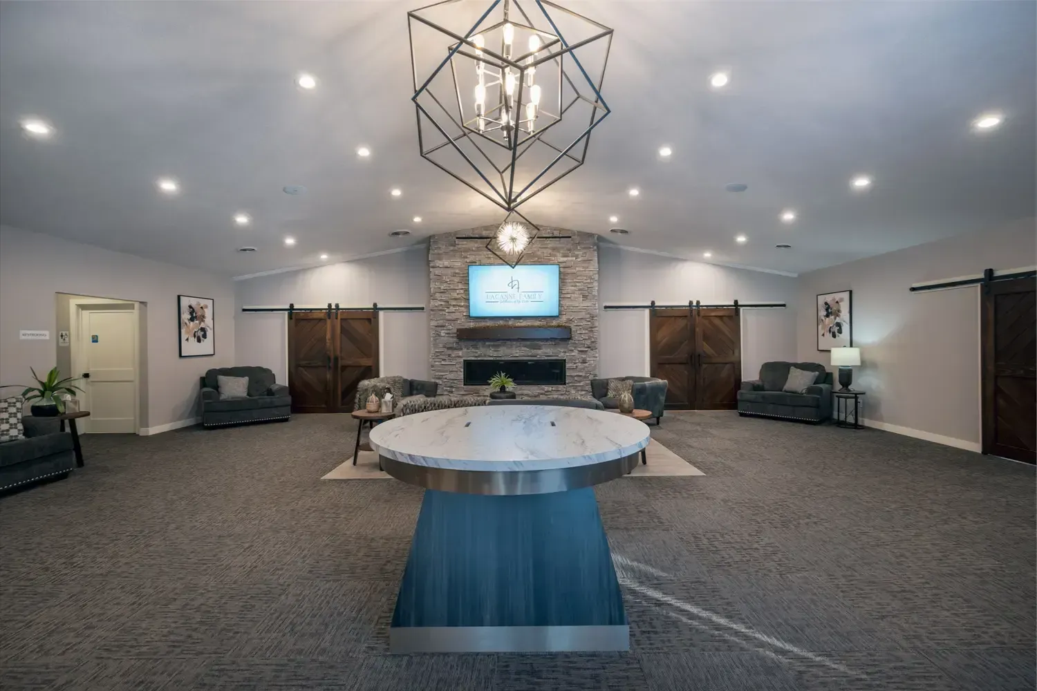Modern lobby with chandelier, TV, seating, and round table on carpeted floor