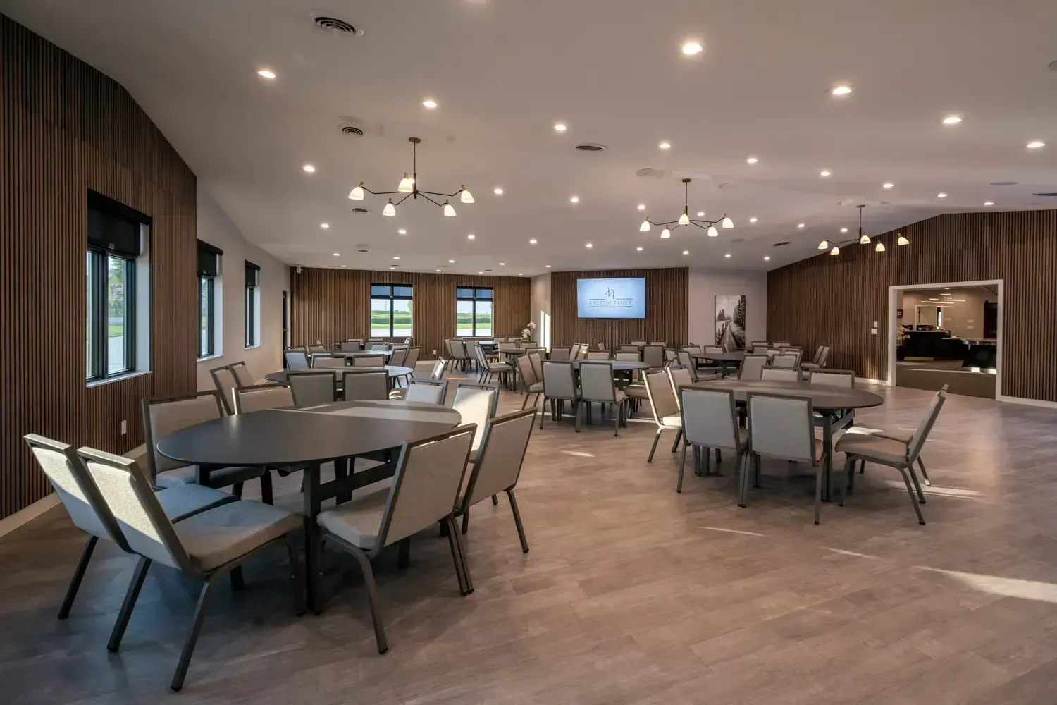Modern dining room with round tables, gray chairs, wood-paneled walls, and recessed ceiling lights