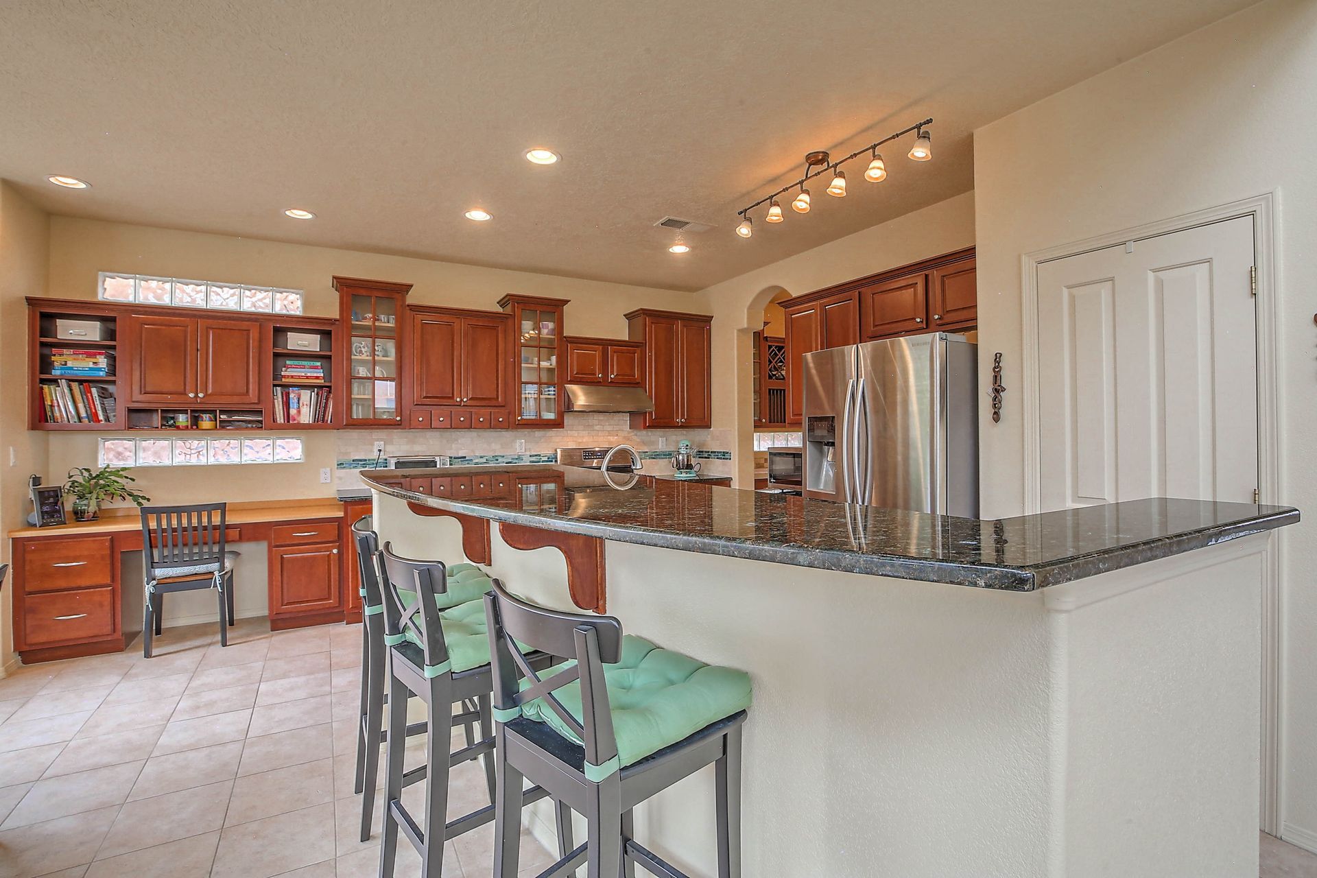 Spacious kitchen with wooden cabinets, granite breakfast bar, and three green stools