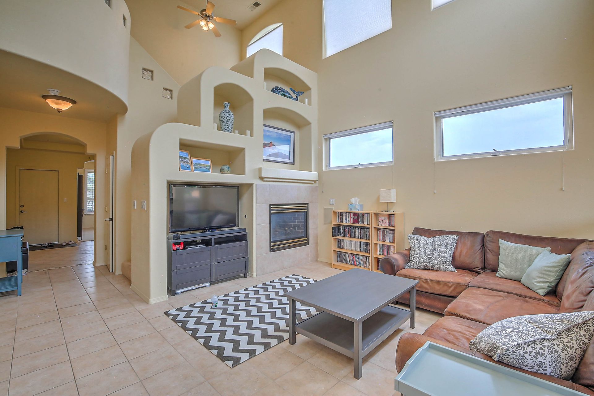 Bright living room with tan sectional sofa, fireplace, zigzag rug, coffee table, and built-in shelves.