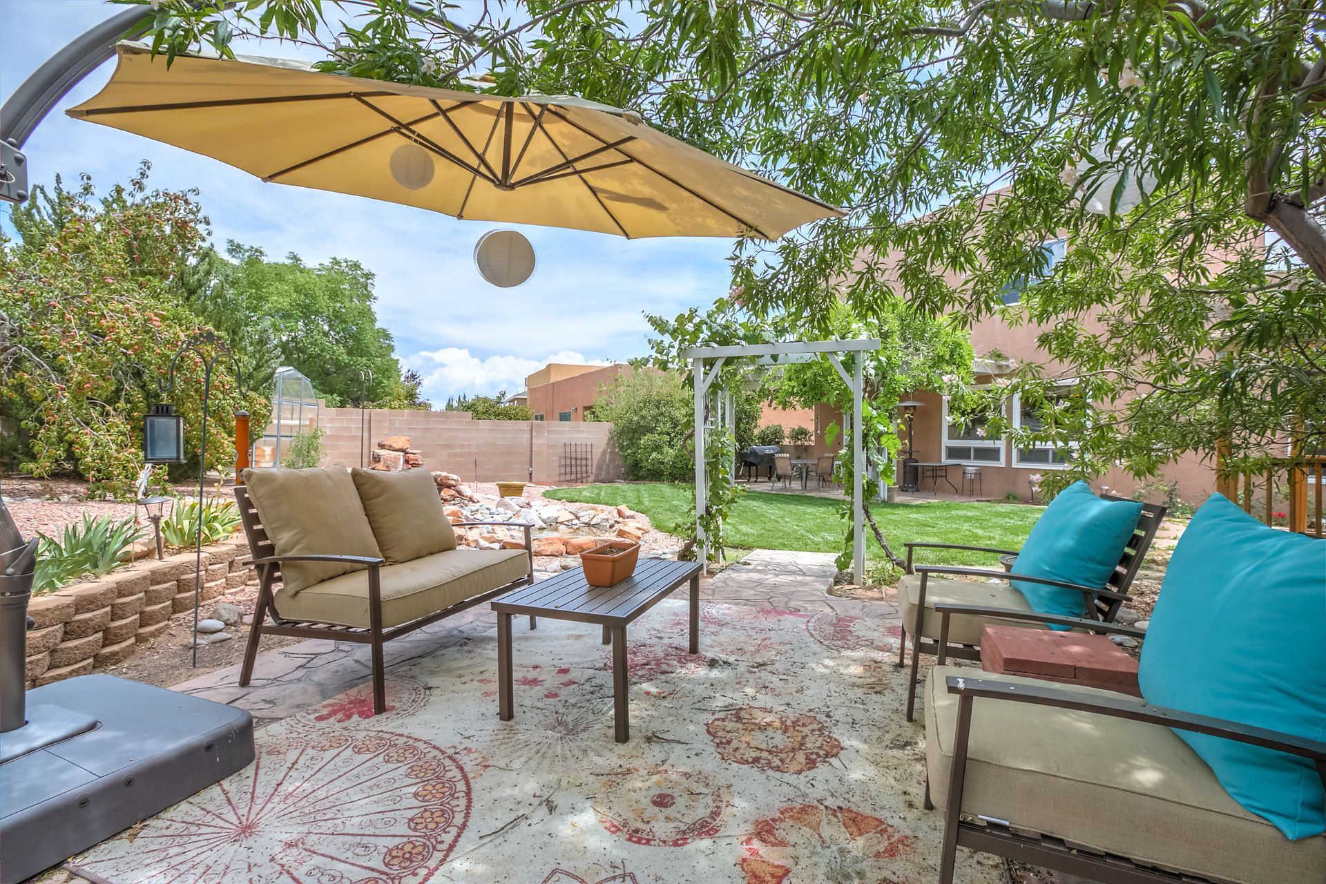 Shaded patio with outdoor sofa, chairs, umbrella, rug, and garden views