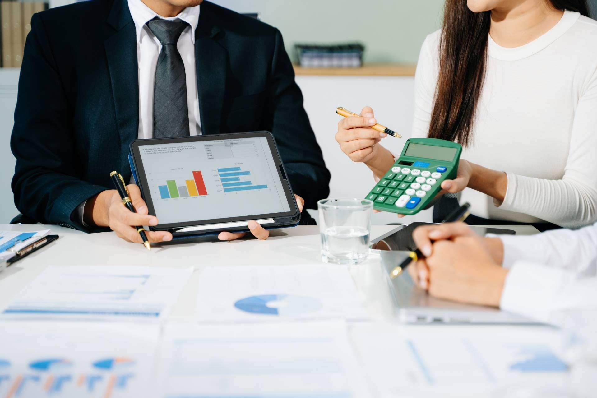 Business meeting with people reviewing charts on a tablet and calculator at a desk