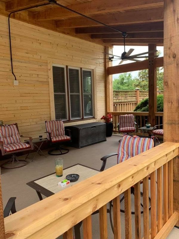 Covered patio with seating, wooden features, and a view of a backyard.