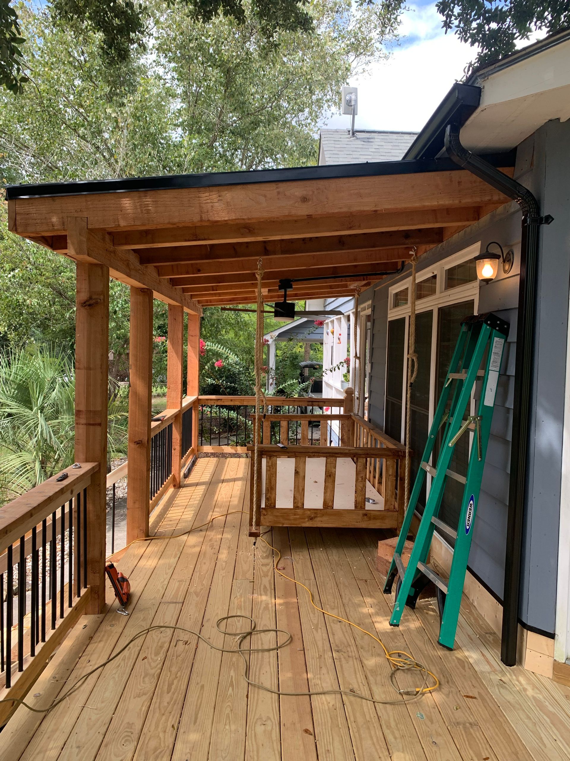 Wooden deck with a porch under construction. Green ladder leans against the wall.